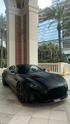 a black sports car parked in front of a tall building with palm trees behind it