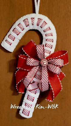 a red and white christmas ornament hanging from a wooden table with ribbon on it