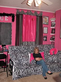 a woman sitting on top of a zebra print couch in a living room with pink walls