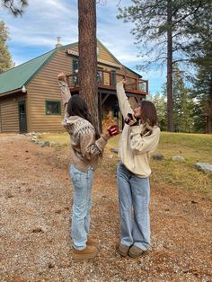 two women standing next to each other in front of a tree with their hands up