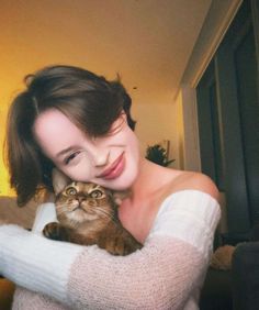 a woman holding a cat in her arms and smiling at the camera while wearing a white sweater