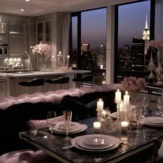 a dining room table with candles and plates on it in front of large windows overlooking the city