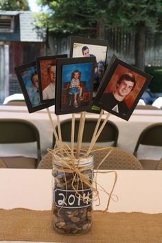 a mason jar filled with pictures on top of a table next to a wooden stick