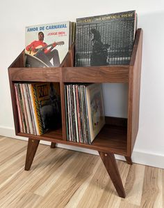 a wooden shelf filled with vinyl records on top of a hard wood floor next to a white wall