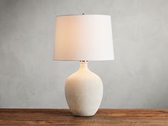 a white lamp sitting on top of a wooden table next to a light gray wall