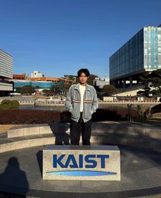 a young man standing in front of a sign that says kaist with buildings in the background