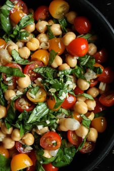 a salad with tomatoes, chickpeas and spinach in a black bowl on a table