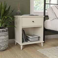 a white nightstand sitting next to a bed with a plant on top of it in a bedroom