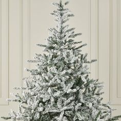 a small white christmas tree with snow on it's branches in front of a wall