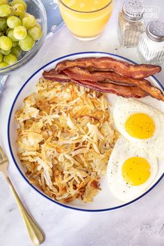 a plate with eggs, hash browns and bacon on it next to glasses of orange juice