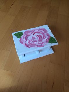 a white box with a pink flower painted on the lid sitting on a wooden floor