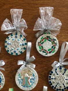 six ceramic ornaments with ribbons tied around them on a wooden surface, all decorated in different designs and colors