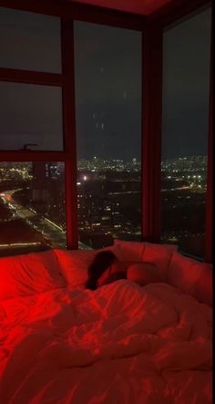 a person laying on top of a bed in front of a window with red light