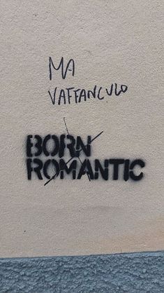 graffiti written on the side of a building in front of a wall with writing that reads born romantic