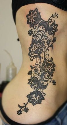 a woman's lower back tattoo with flowers and vines on her side ribcage