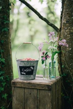 two vases with flowers in them sitting on a wooden box next to a tree