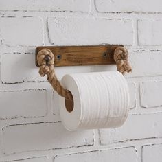 a roll of toilet paper hanging from a wooden holder on a brick wall with two rope wrapped around it