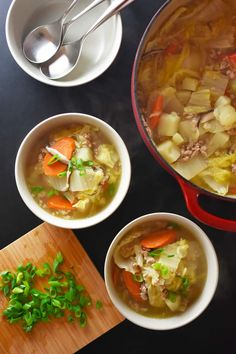 three bowls filled with soup next to a cutting board and spoons on a table