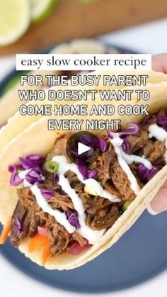 a hand holding a taco with shredded meat and coleslaw on it, in front of a plate