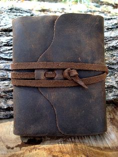 a brown leather journal sitting on top of a piece of wood with a knot around it