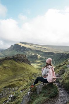 a woman sitting on top of a hill next to a lush green hillside