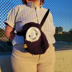 a woman wearing a crocheted backpack with a smiling face on the front pocket