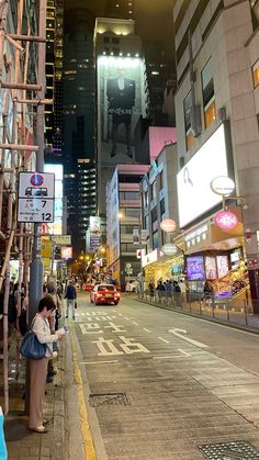 people are standing on the sidewalk in front of tall buildings at night, with one person using her cell phone