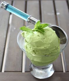 a scoop of green ice cream in a glass bowl with a spoon on a wooden table