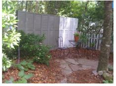 an outdoor patio with table and chairs next to a fenced in area surrounded by trees