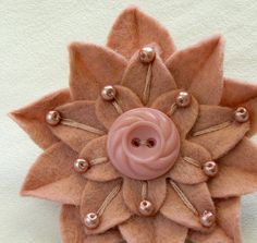 a pink flower brooch with pearls on it sitting on a white table cloth covered surface