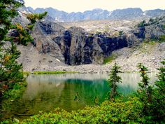 a mountain lake surrounded by trees and mountains in the distance with green water on both sides