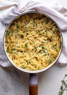 a pot filled with pasta and parsley on top of a white table cloth next to a wooden spoon