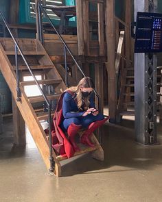 a woman in a red and blue suit sitting on a chair looking at her cell phone