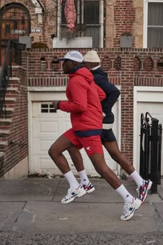 two men are running on the sidewalk in front of a house