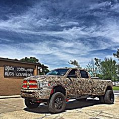 a camo truck parked in front of a brick building under a cloudy blue sky