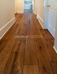 an empty hallway with wood floors and white doors on both sides, leading to another room