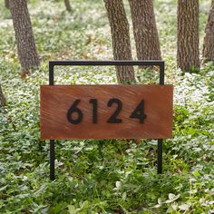 a wooden sign sitting in the middle of a forest filled with green grass and trees