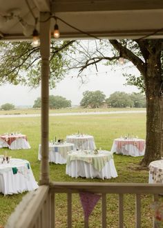 an outdoor dining area with tables and chairs set up under a tree in the grass