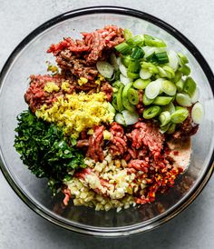 a glass bowl filled with meat, vegetables and seasoning sitting on top of a table