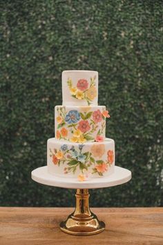 a three tiered cake with flowers painted on the side is sitting on a wooden table