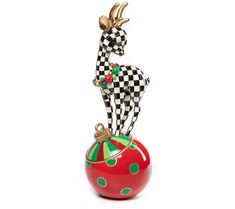 a ceramic figurine sitting on top of a red apple with a green and white checkerboard design