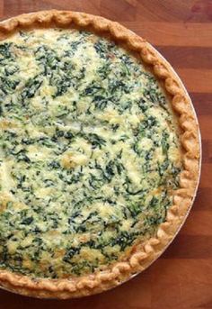 a quiche with spinach and cheese in a pie pan on a wooden table