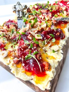 a pizza with cranberry sauce, nuts and herbs on it sitting on a cutting board