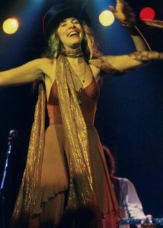 a woman in a dress and hat on stage with her arms spread out to the side