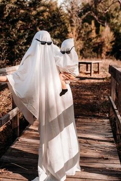 two people in white robes walking across a wooden bridge with their heads covered by coverings