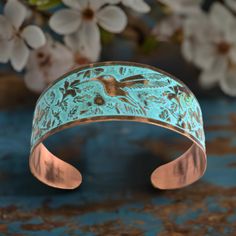 a close up of a bracelet on a table with flowers in the background and a bird painted on it