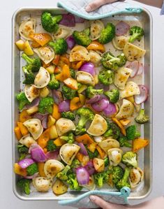 a pan filled with vegetables on top of a white table next to a person's hand