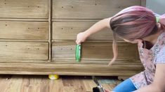 a woman sitting on the floor with a brush in her hand next to a dresser