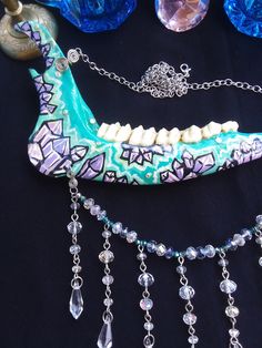 This is a Beautiful Painted,Turquoise Crystal Deer Jawbone Necklace! The Colors Here Are Just Fantastic! The Painted crystals Are a Light Purple Color And The Backdrop is Turquoise! A few rhinestones as well. Hanging from the bottom is a String of Glass beads! All 6 Teeth Are in perfect condition. The Whole Jaw Bone is 9 inches long. Also coated with polyurethane for the beautiful shine. The Chain is 20 inches long. All Items Ship Within 1-3 Days via USPS First Class Service. Shipping on This Bo Bohemian Bone-colored Necklace For Festivals, Unique Handmade Bone-colored Necklace, Handmade Bone-colored Unique Necklace, Unique Handmade Bone Necklace, Bohemian Bone Colored Jewelry For Festivals, Bohemian Bone-colored Jewelry For Festival, Painted Crystals, Real Bone Jewelry, Wiccan Necklace