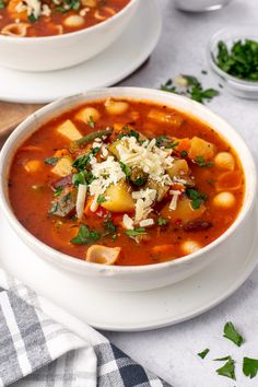 two bowls of vegetable soup with parmesan cheese on top and another bowl in the background